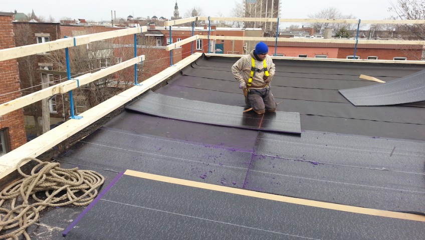 Exterior view of a professional roofer roofing on the flat roof of a building