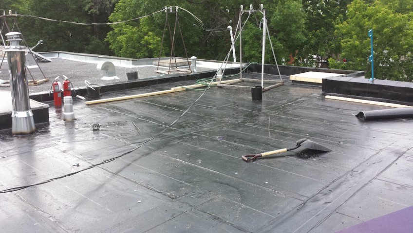 Vue extérieure d'un toit plat montrant l'application et l'installation d'une toiture élastomère par des couvreurs professionnels.